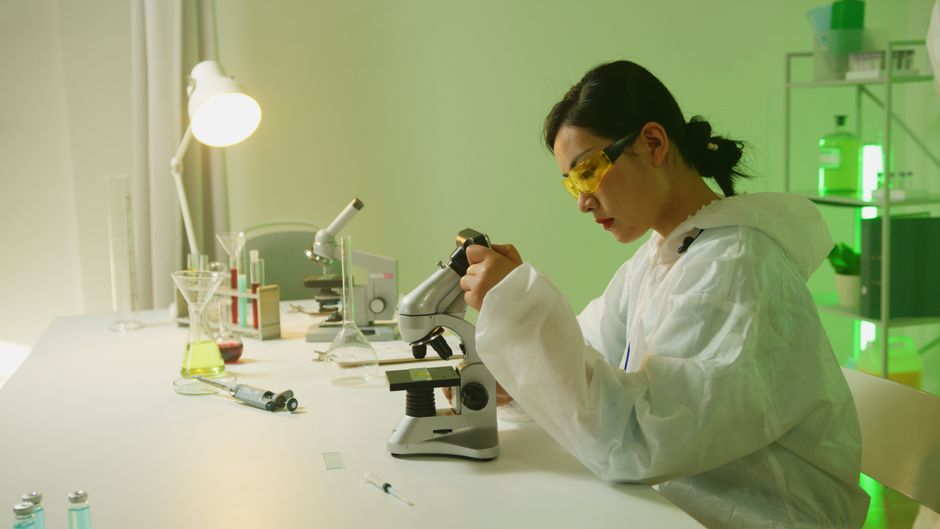 A scientist in a laboratory uses a microscope for research. Indoor lab setting.