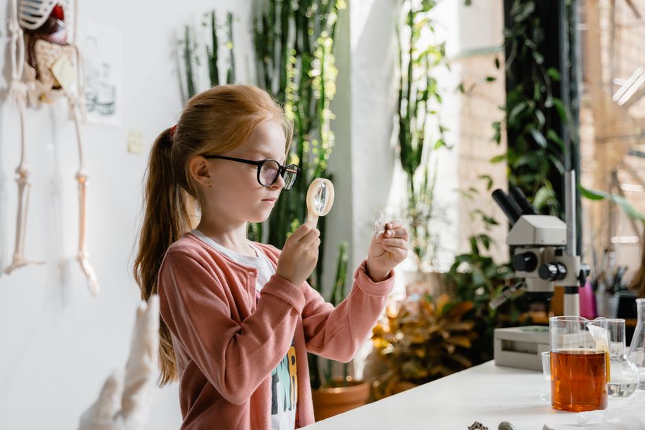 A young girl uses a magnifying glass to study samples in a vibrant indoor lab environment.