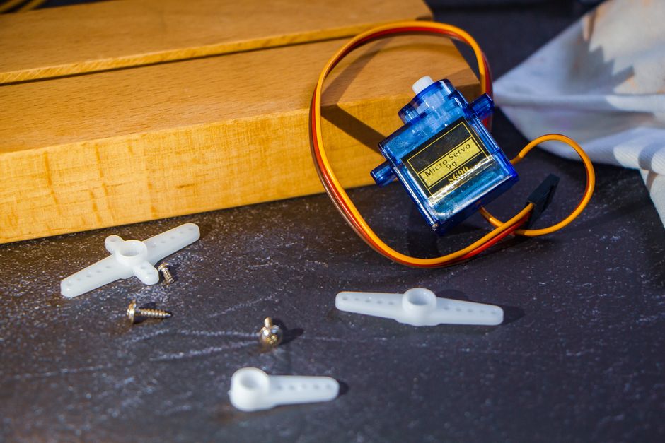 Close-up of a micro servo motor with plastic arms and screws on a workbench, ideal for robotics projects.
