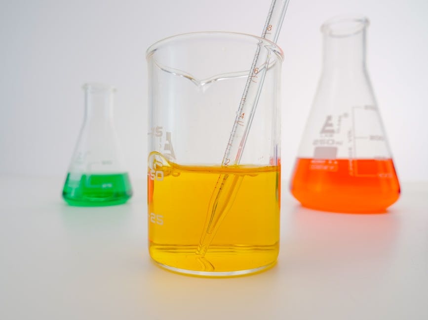 Close-up of vibrant chemical solutions in beakers with pipette in a lab setting.