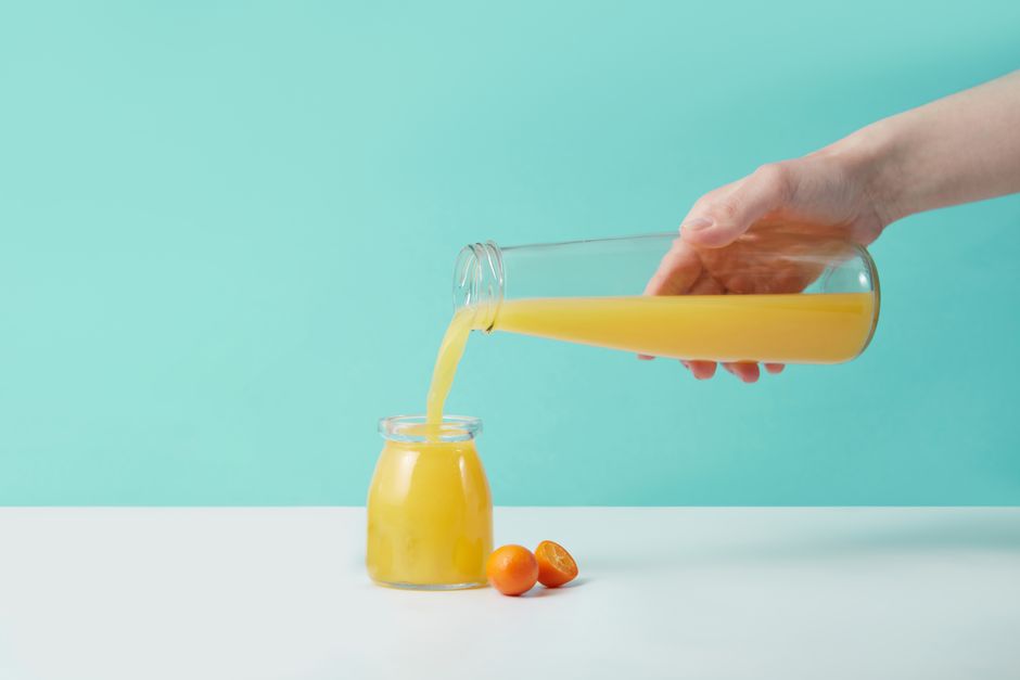 Refreshing orange juice being poured from a glass pitcher into a jar, set against a turquoise background.