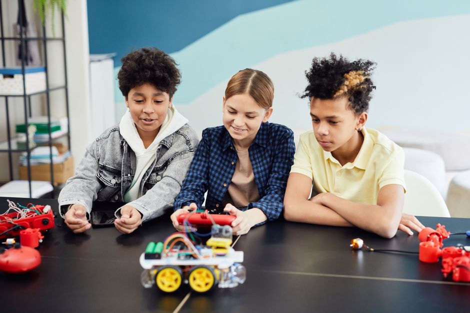 Teens exploring and building robotics at a table indoors, showcasing teamwork and technology skills.