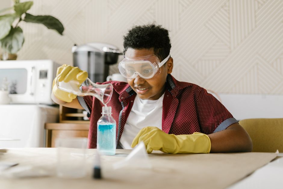 Young boy engaged in a home science experiment, pouring liquid with safety goggles.
